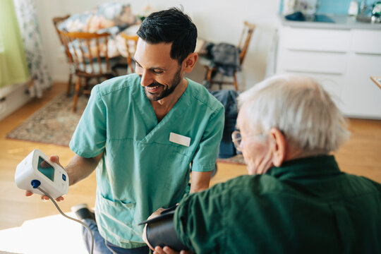 Smiling male nurse examining blood pressure of senior man at retirement home