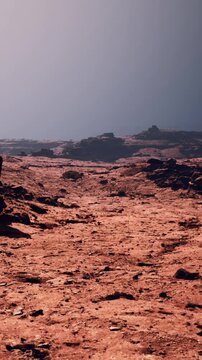 A vast red terrain stretches across the scene with rocky formations scattered throughout. The sky shows a mix of colors as the sun sets. This location appears dry and barren.