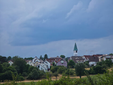 germany, striking church steeple and village skyline of ostfildern kemnat beneath dark thunderstorm clouds above green summer fields