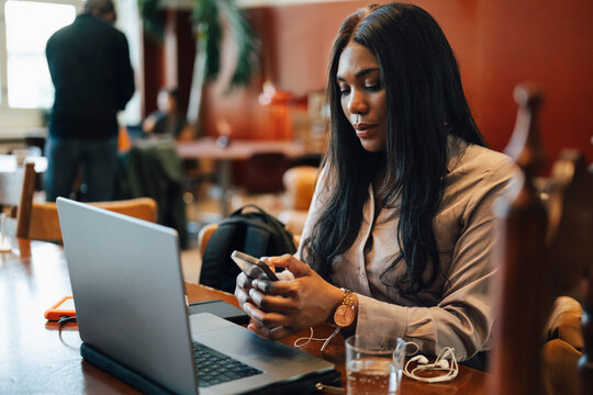 Female entrepreneur text messaging through smart phone during her work session at shared workspace