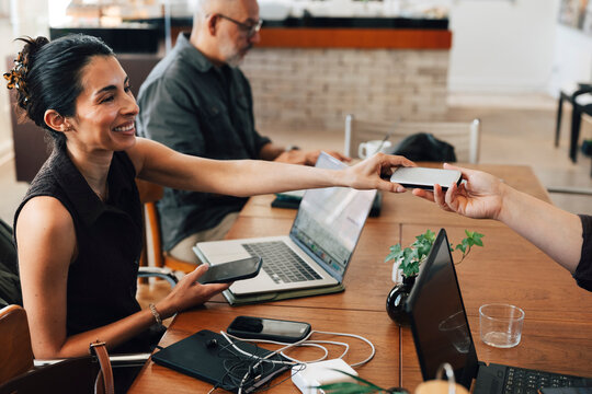 Smiling female entrepreneur sharing her hard drive with coworker while working at coworking space
