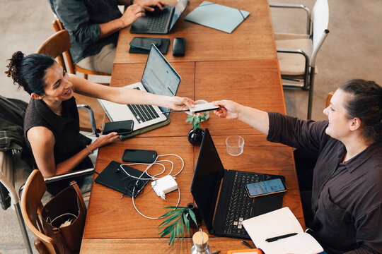 High angle view of female entrepreneur sharing her external hard drive with colleague sitting at desk in coworking space