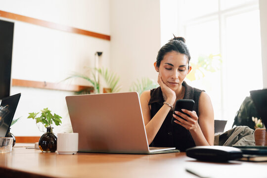 Female entrepreneur checking smart phone while taking break from her work session at modern coworking space