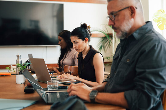 Group of freelancers working independently on laptops while sitting side by side at coworking space desk
