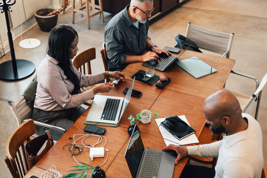 High angle view of freelancers using laptops and electronic gadgets while sitting at large table