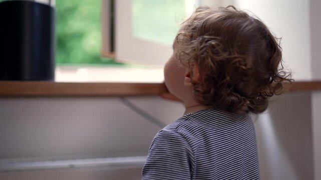 Toddler attempting to close open window at home, highlighting childhood curiosity, independence and early learning