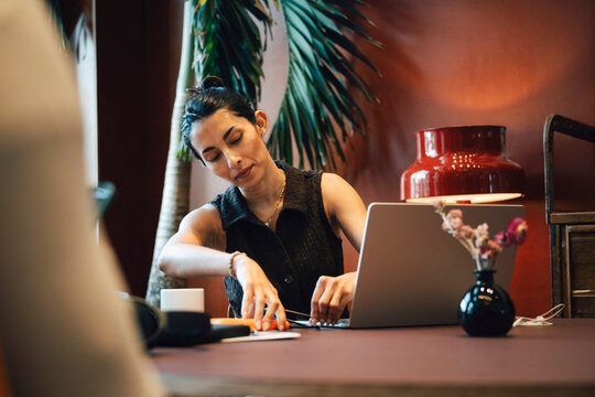 Businesswoman connecting external hard drive to her laptop while sitting at desk in coworking lounge