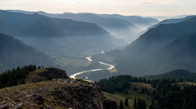 Misty mountain valley and winding river viewed from rocky clifftop