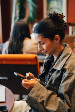 Businesswoman using smart phone while sitting in coworking space lounge