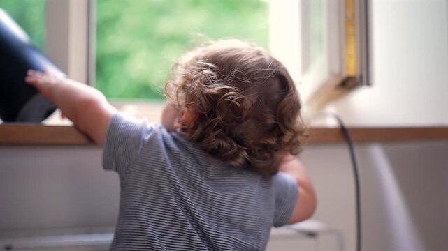 Toddler knocking object off windowsill at home, highlighting childhood curiosity, cause and effect learning and early development