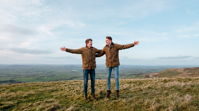 Two joyful men with open arms celebrating on green hilltop vista