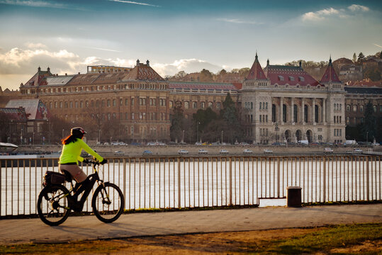 Cyclist riding along the Danube river embankment with the Budapest University of Technology and Economics in the background, Hungary