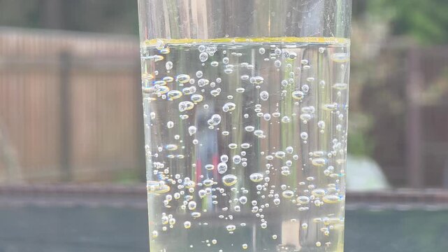 Bubbles rising in a glass of sparkling water outdoors on a sunny day