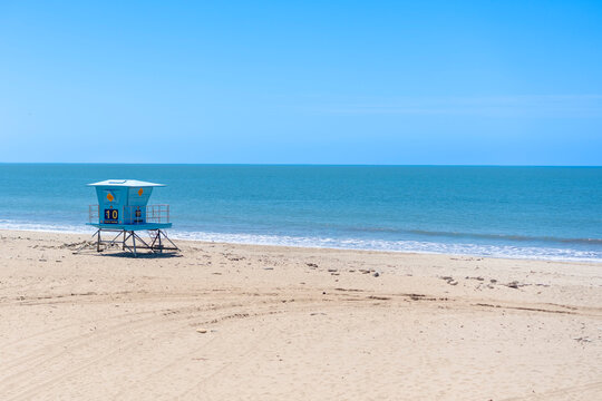 View of a blue lifeguard tower standing on the sandy beach facing the blue ocean horizon under a clear sky in California