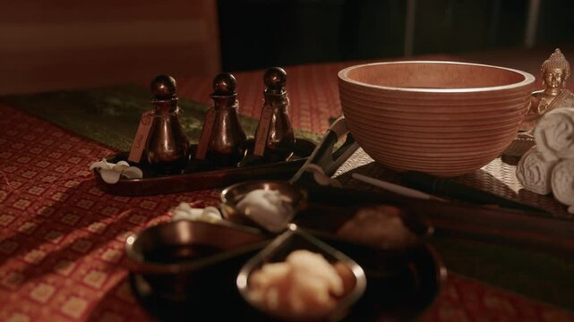 Tracking shot of wooden bowl and massage oil bottles arranged on spa treatment table in dim interior slow smooth pan.