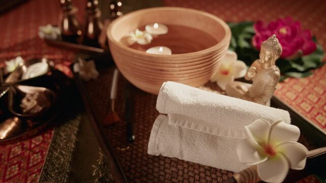Top view spa arrangement with rolled towel bowl floating candles and frangipani on woven mat.