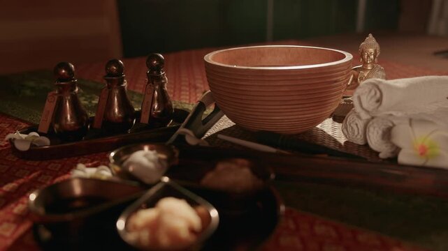 Slow pushin of wooden bowl and spa accessories arranged on massage table in dim treatment room.