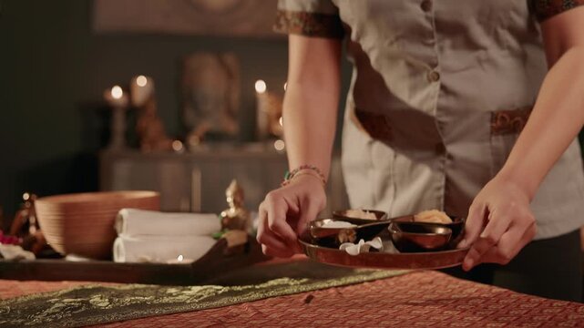 Slow motion Thai therapist placing aromatherapy tray on massage table in spa treatment room.