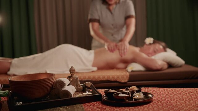Slow motion Thai therapist massaging client on spa bed in dim treatment room.