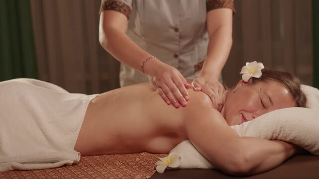 Slow motion woman receiving back massage on spa treatment table in warm treatment room.