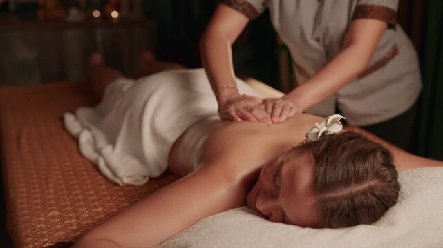 Slow motion woman receiving back massage by masseuse in spa treatment room on treatment table, top view.