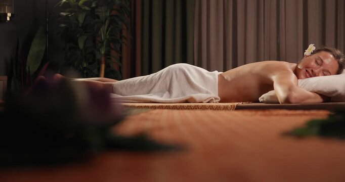 Slow motion woman receiving Thai massage on mat in spa treatment room with low tracking dolly movement across foreground.