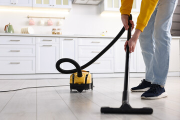 Fototapeta premium Housework. Teenage boy cleaning floor with vacuum cleaner in kitchen, closeup