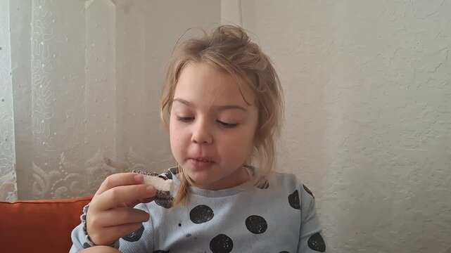Child enjoys sweet treat at home while sitting on a couch during afternoon time with family nearby