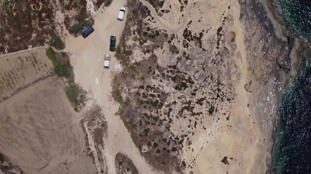 Salt Evaporation Ponds Off the Coast of Gozo, Malta. Xatt L-Ahmar road, parking and agricultural land. aerial view of a coastal road with sandy terrain and water body in a neutral. High quality 4k