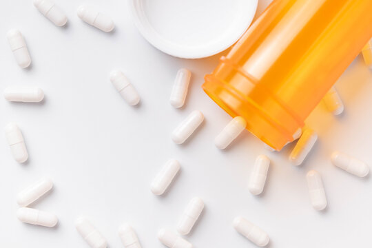 White capsules spilled out of an orange bottle, scattered over a white background