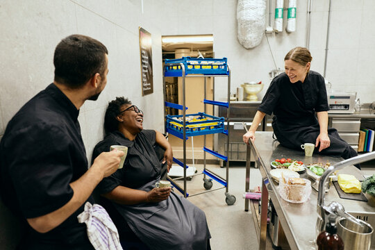 Happy kitchen team laughing while having coffee during their shift