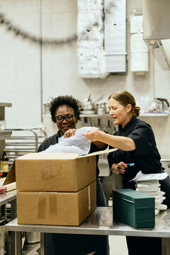 Two female chefs opening delivery boxes together in commercial kitchen
