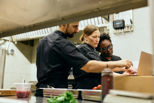 Professional chefs using laptop placed on cardboard box during restaurant service