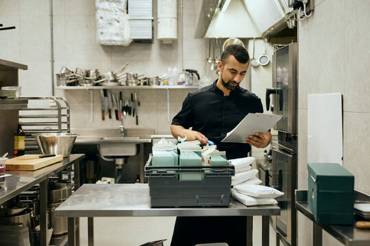 Male chef counting delivered stock while standing in commercial kitchen