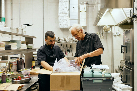 Two male chefs opening delivery boxes in restaurant kitchen