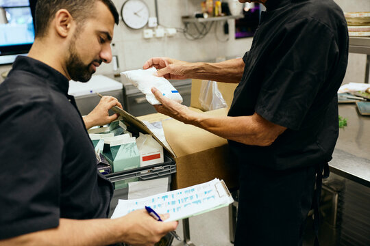 Two male chefs taking stock inventory in modern commercial kitchen