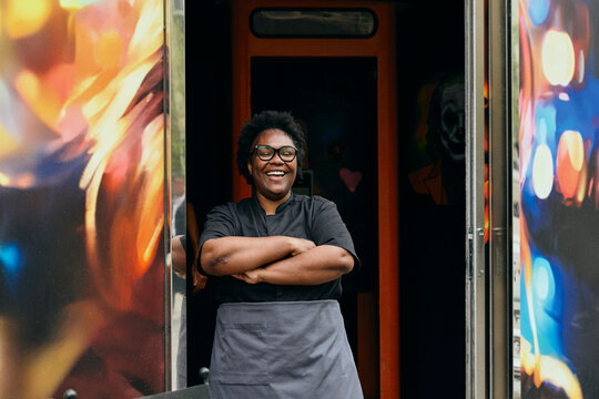 Portrait of happy female chef posing with arms crossed at restaurant entrance