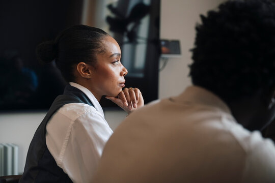 Side view of female employee sitting with hand on chin during office meeting