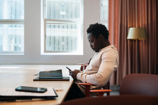 Side view of male entrepreneur using smart phone while sitting on chair in meeting room