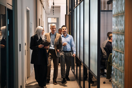 Diverse business partners discussing while walking in office hallway