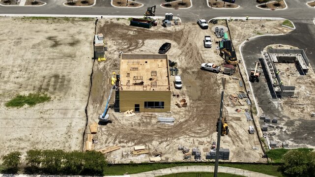 Aerial view of a construction site featuring a building under construction, heavy machinery, and dirt ground in World Golf Village, Florida, United States.