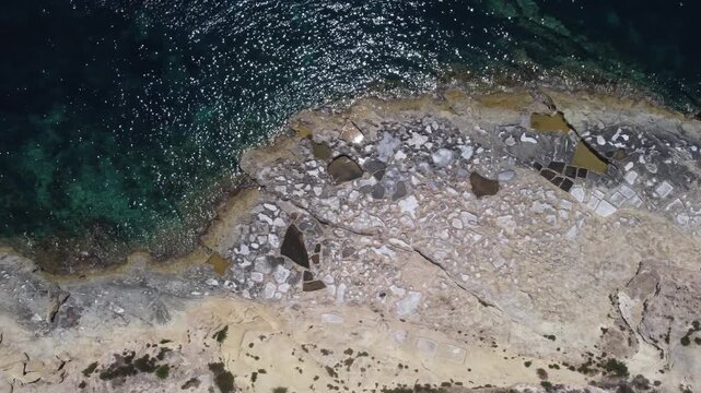 Xatt L-Ahmar, salt pans, Gozo island, Malta. serene aerial view of rocky coastline with clear blue ocean waves and sandy shorelines during a peaceful vacation in nature. High quality 4k footage