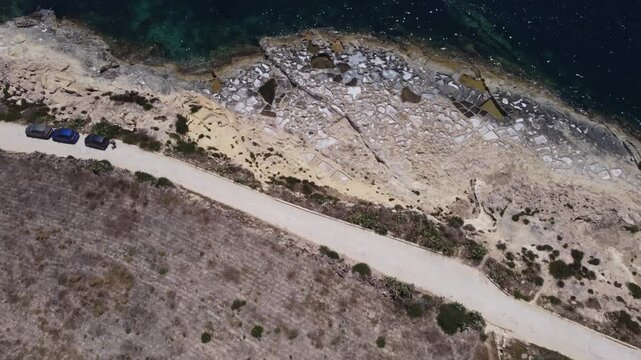 Xatt L-Ahmar, salt pans, Gozo island, Malta. serene aerial view of rocky coastline with clear blue ocean waves and sandy shorelines during a peaceful vacation in nature. High quality 4k footage
