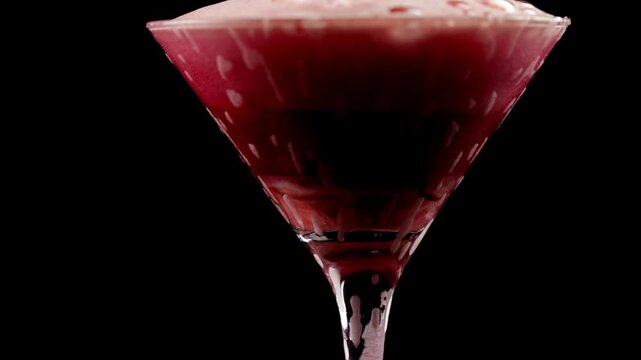 Foamy drink in a transparent glass on a black background, red foamy drink in a martini glass