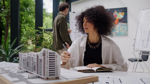 Female architect analyzes detailed model of apartment building
