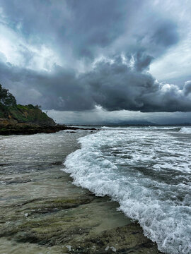 Aerial view of the rocky coastline and crashing waves under dramatic dark storm clouds at Byron Bay, New South Wales, Australia.