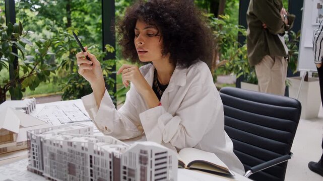 Lady architect carefully studies apartment complex model at table