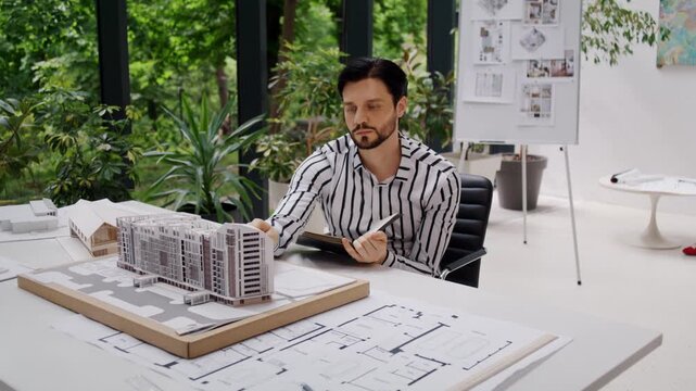 Engineer checks multistory building model and notes in office