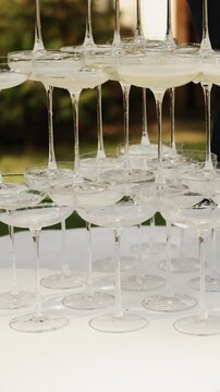 Vertical video. Bride and groom pour champagne into a glass pyramid during their wedding celebration.