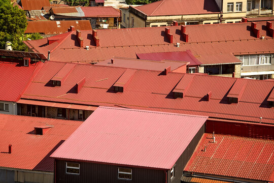 High angle view of dense residential district houses featuring red corrugated steel roofing, chimneys, firewall parapets and roof access hatches.